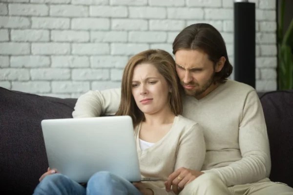 young couple looking at computer monitor and upset about online scam